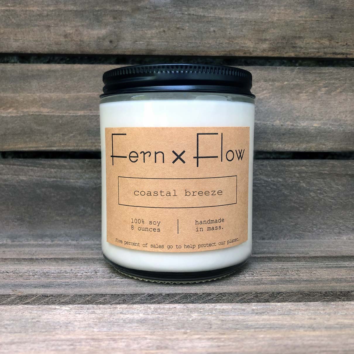Fern x Flow Coastal Breeze summer-time scented soy candle against a rustic wooden background.